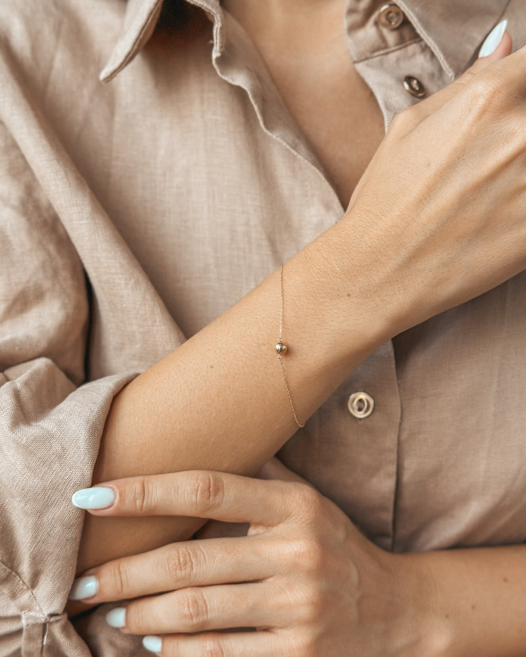 Gros plan d'une personne portant un bracelet en or délicat au poignet, avec une manche de chemise beige soulignant l'élégance de l'accessoire.