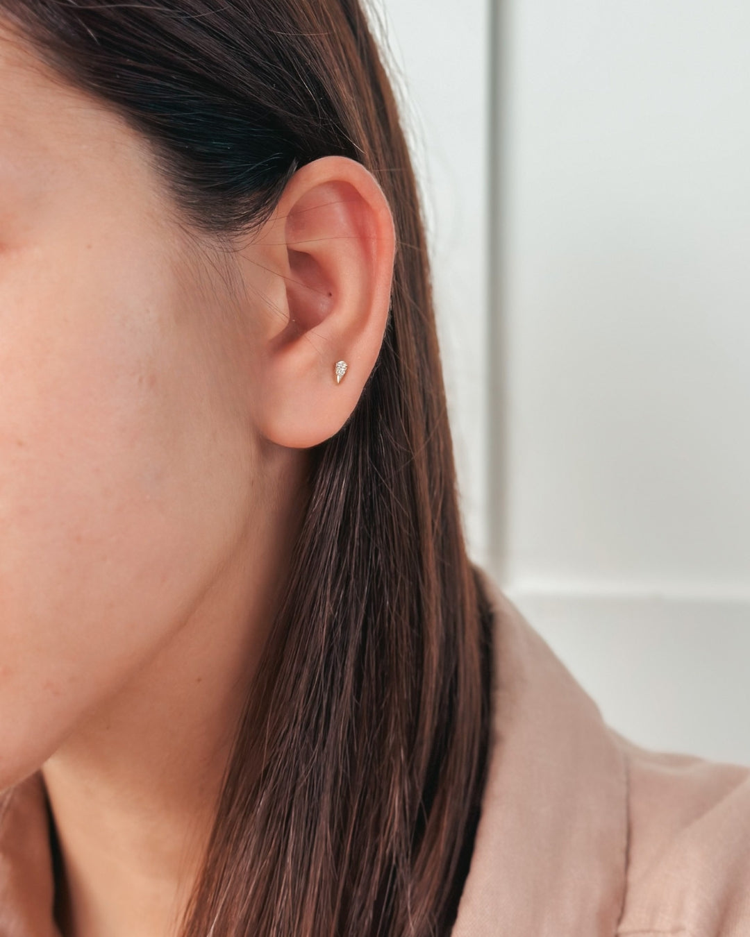 Gros plan sur une oreille ornée d'une petite boucle d'oreille sur un fond clair.