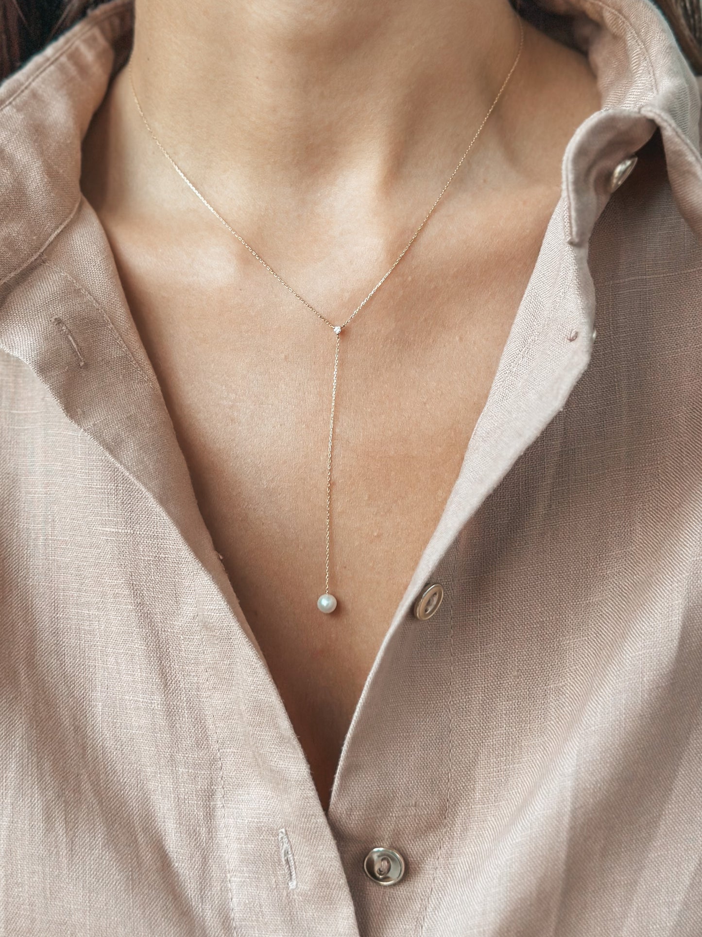 Gros plan d'un collier en or délicat avec un pendentif perle porté sur une chemise à col ouvert.