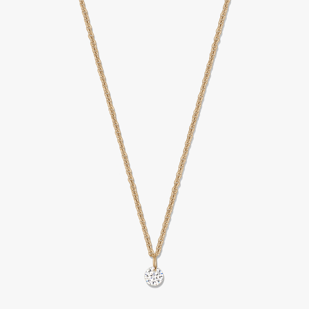 Collier en argent doré avec pendentif solitaire rond en oxyde de zirconium clair, sur fond blanc.