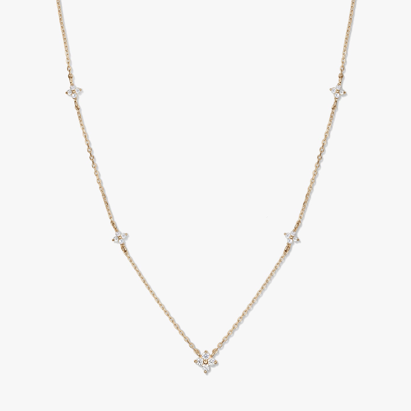 Collier délicat en or jaune 14K de type station, avec de petits motifs trèfle en zirconia blanc sur une chaîne fine, photographié sur fond blanc.