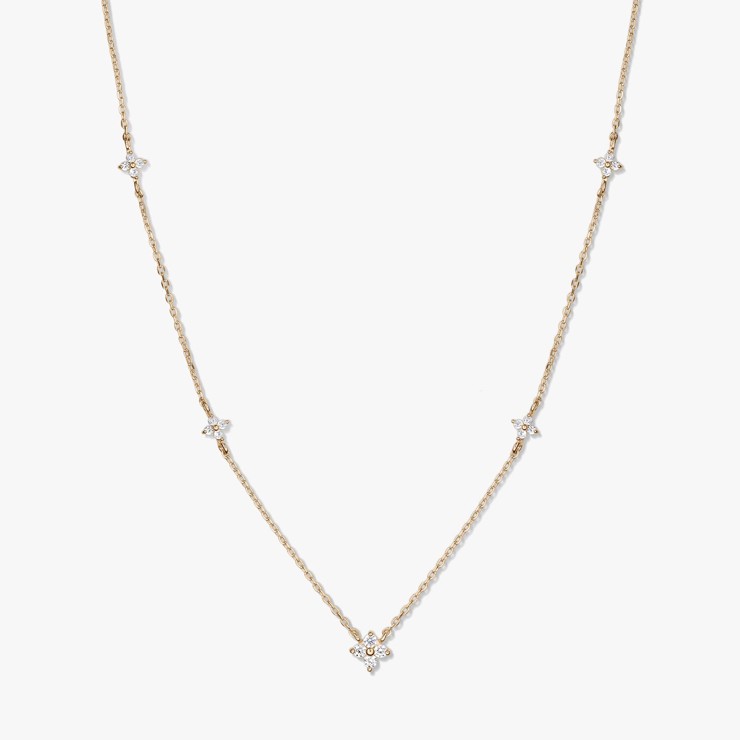 Collier délicat en or jaune 14K de type station, avec de petits motifs trèfle en zirconia blanc sur une chaîne fine, photographié sur fond blanc.