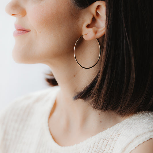 Gros plan de profil d’un mannequin portant une grande créole en or jaune 14k, présentée à l’oreille sous une douce lumière naturelle.