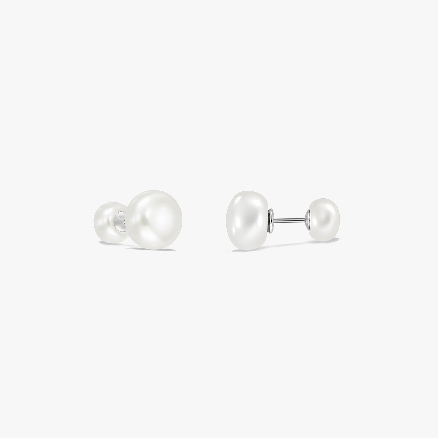 Paire de boucles d’oreilles puces à double perle en argent sterling sur fond blanc, chacune avec une grande perle naturelle blanche à une extrémité et une plus petite à l’autre, reliées par une tige.