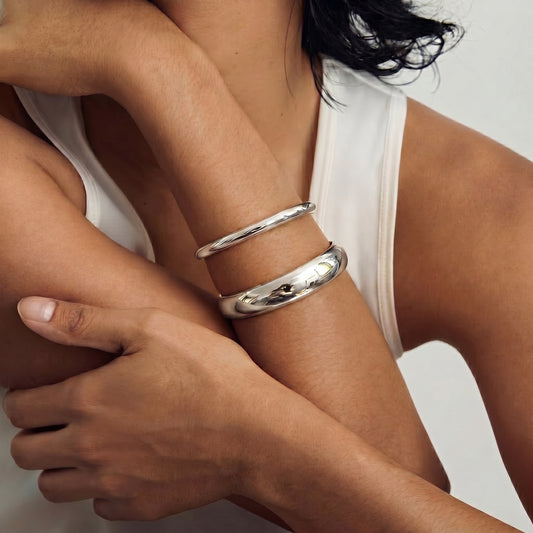 Une personne portant deux bracelets en argent sur le bras, posée contre un fond neutre.