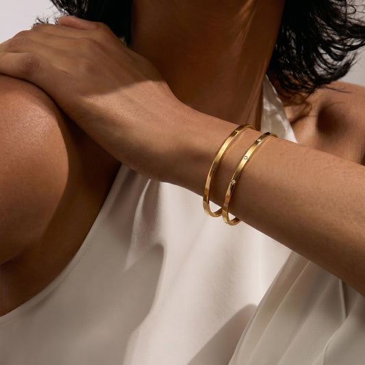 Gros plan sur le bras d'une personne portant deux bracelets en or sur fond blanc.