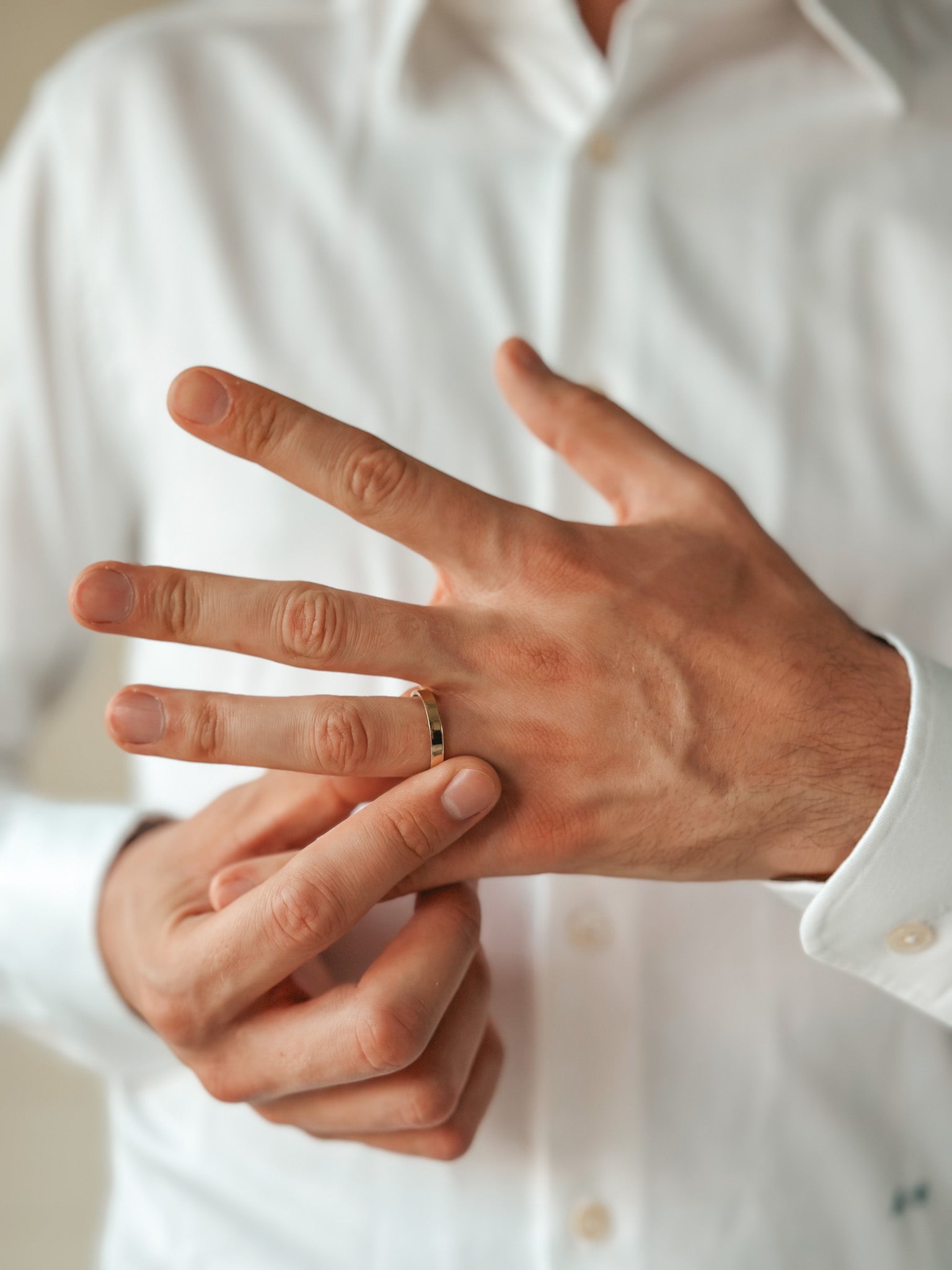 Une personne en chemise blanche mettant une alliance en or simple à son doigt.