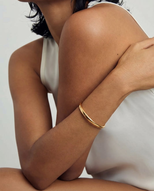Gros plan sur une personne portant un bracelet en argent doré au bras, vêtue d'un haut blanc sans manches.