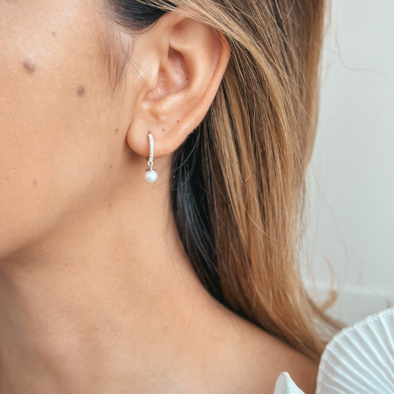 Gros plan sur l’oreille d’une femme portant des boucles d’oreilles en argent ornées d’une perle et de pierres en oxyde de zirconium.
