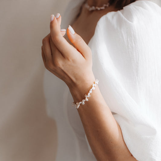 Gros plan d’un poignet portant un délicat bracelet en argent sterling à perles Keshi, photographié en douce lumière naturelle sur une blouse blanche.
