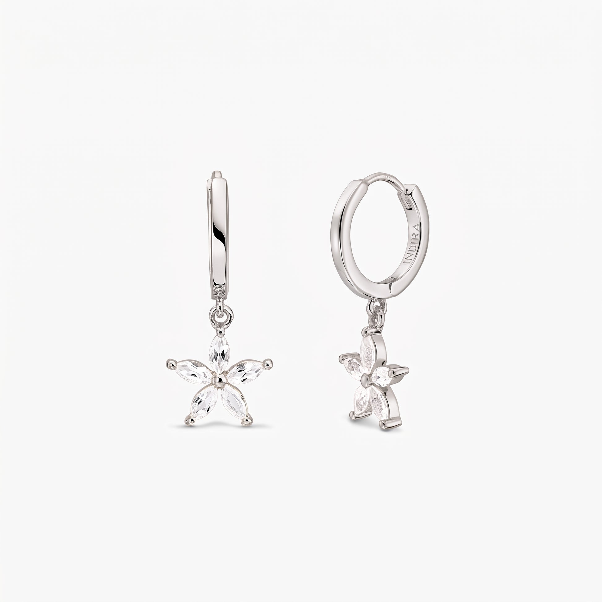 Paire de créoles huggie en argent sterling, ornées de breloques fleur à cinq pétales serties de topaze blanche, sur fond blanc.