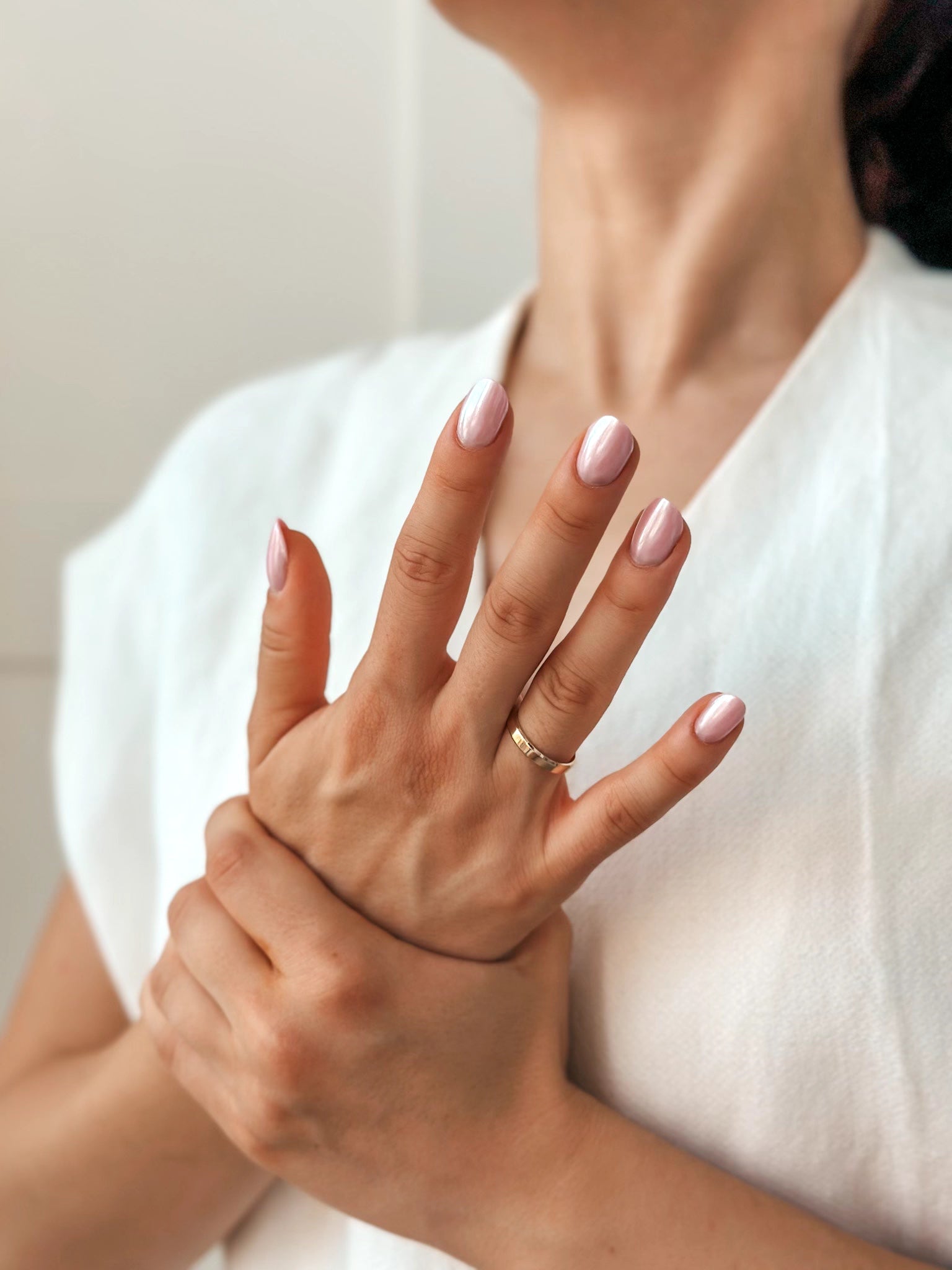 Gros plan sur les mains d'une femme avec un vernis à ongles rose et portant une alliance en or, sur un fond clair.