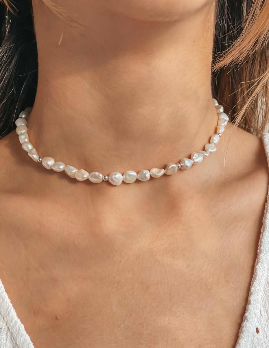 Gros plan sur le cou d'une personne portant un collier en argent avec des perles naturelles.