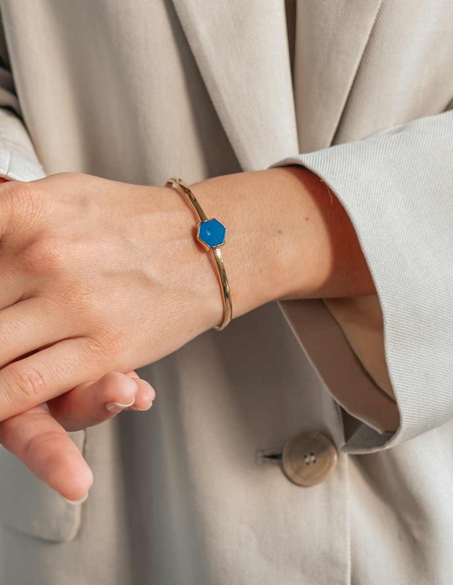 Une main portant un bracelet en argent avec une pierre de lapis-lazuli bleu, sur un fond de vêtement beige clair.