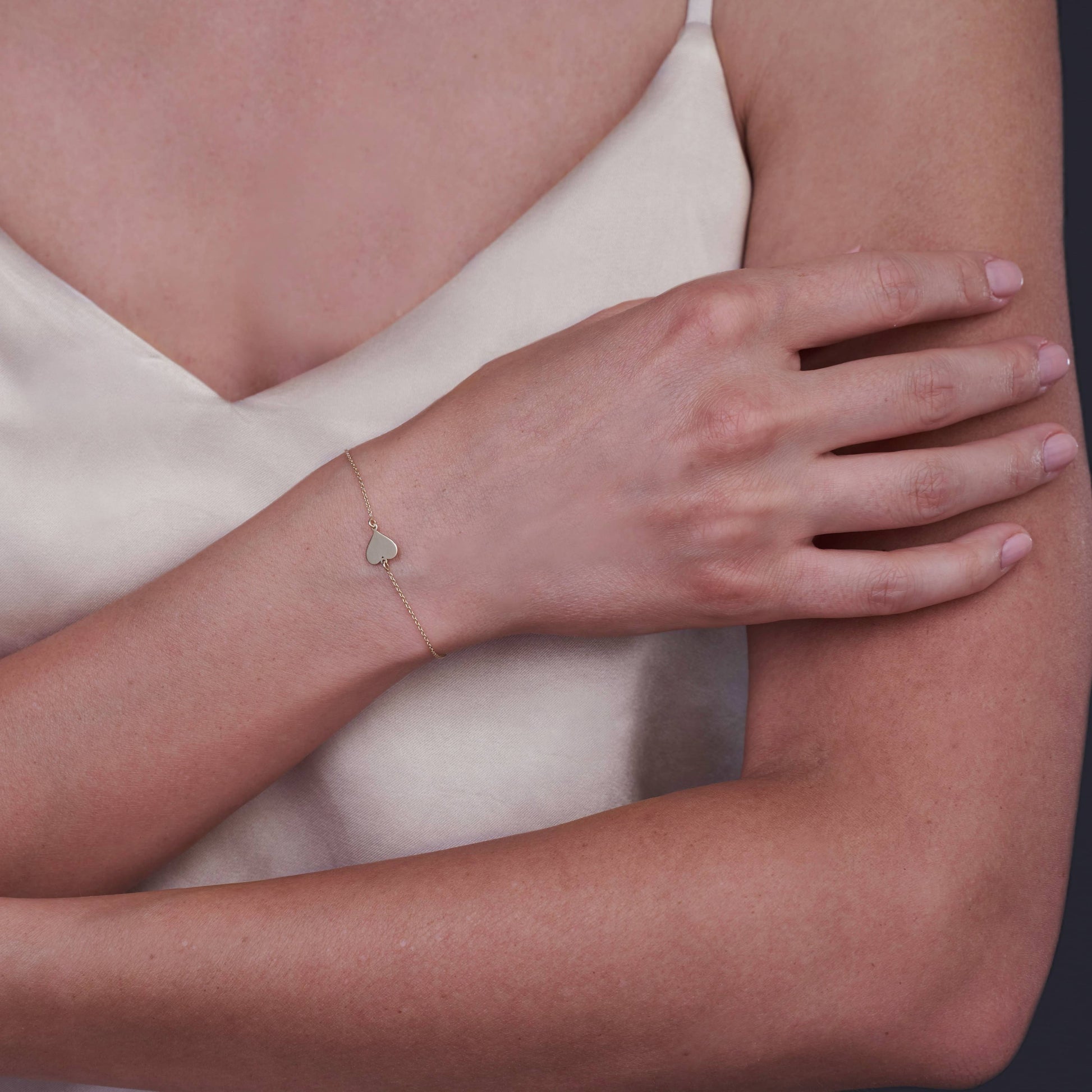 Gros plan sur un poignet portant un bracelet cœur en or 14K au design minimaliste.