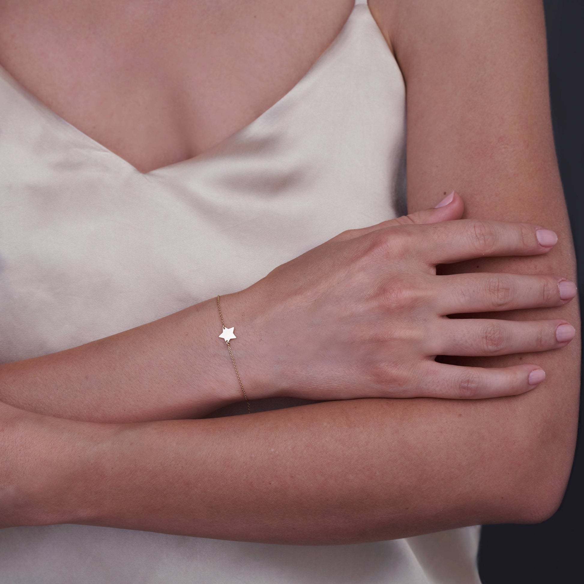 Un bras de femme portant un délicat bracelet étoile en or 14K sur un haut en satin de couleur claire.