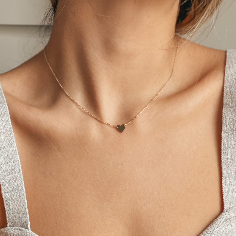 Un cou de femme portant un délicat collier cœur en or 14K.