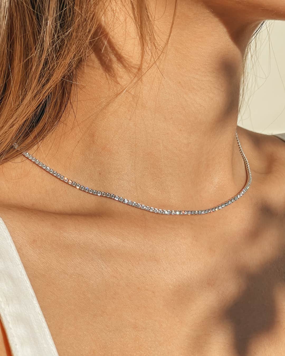 Gros plan sur le cou d'une femme portant un collier tennis en argent avec des pierres de zirconium.