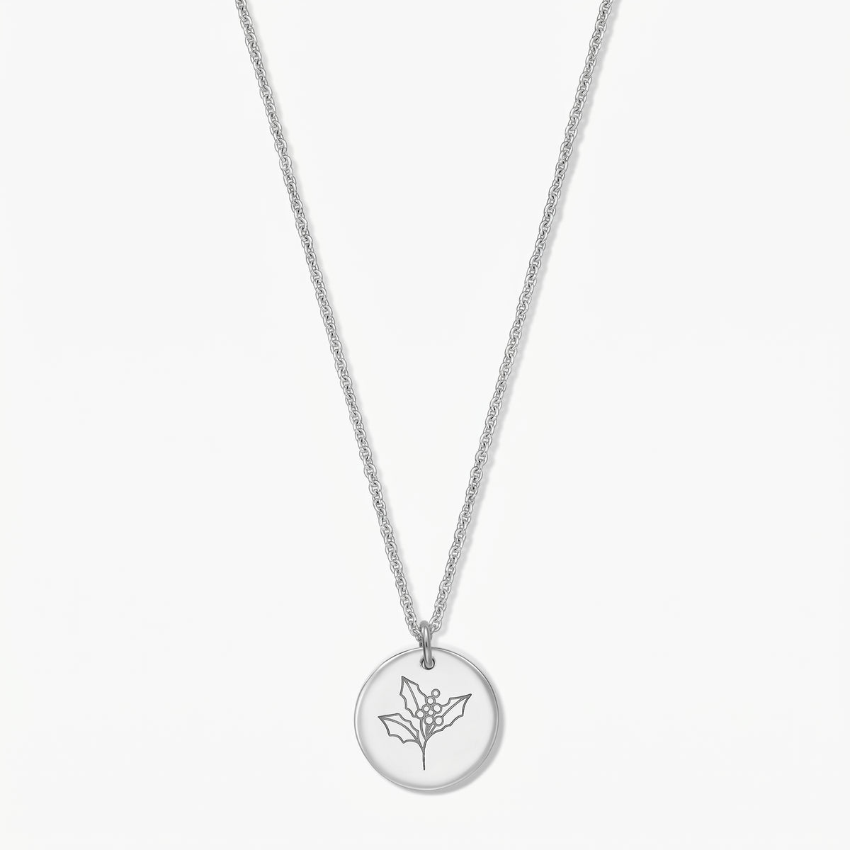 Collier fleur de naissance en argent sterling, pendentif rond gravé d’une branche de houx, présenté sur fond blanc.