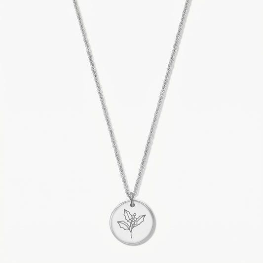Collier fleur de naissance en argent sterling, pendentif rond gravé d’une branche de houx, présenté sur fond blanc.