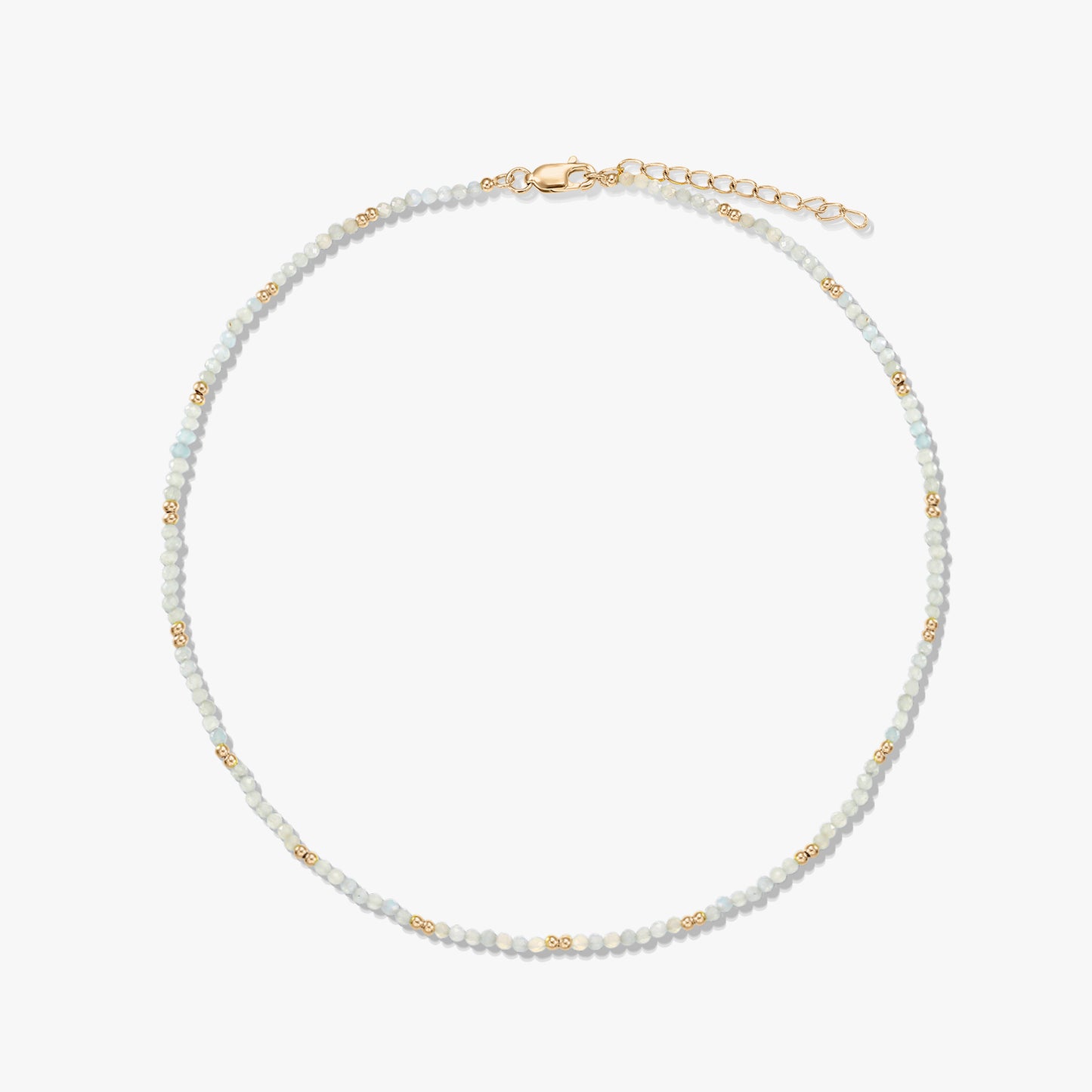 Collier délicat en perles de pierre de lune, rehaussé de petites perles intercalaires dorées, avec fermoir mousqueton et chaînette d’extension en argent sterling plaqué or, disposé en cercle sur fond blanc.