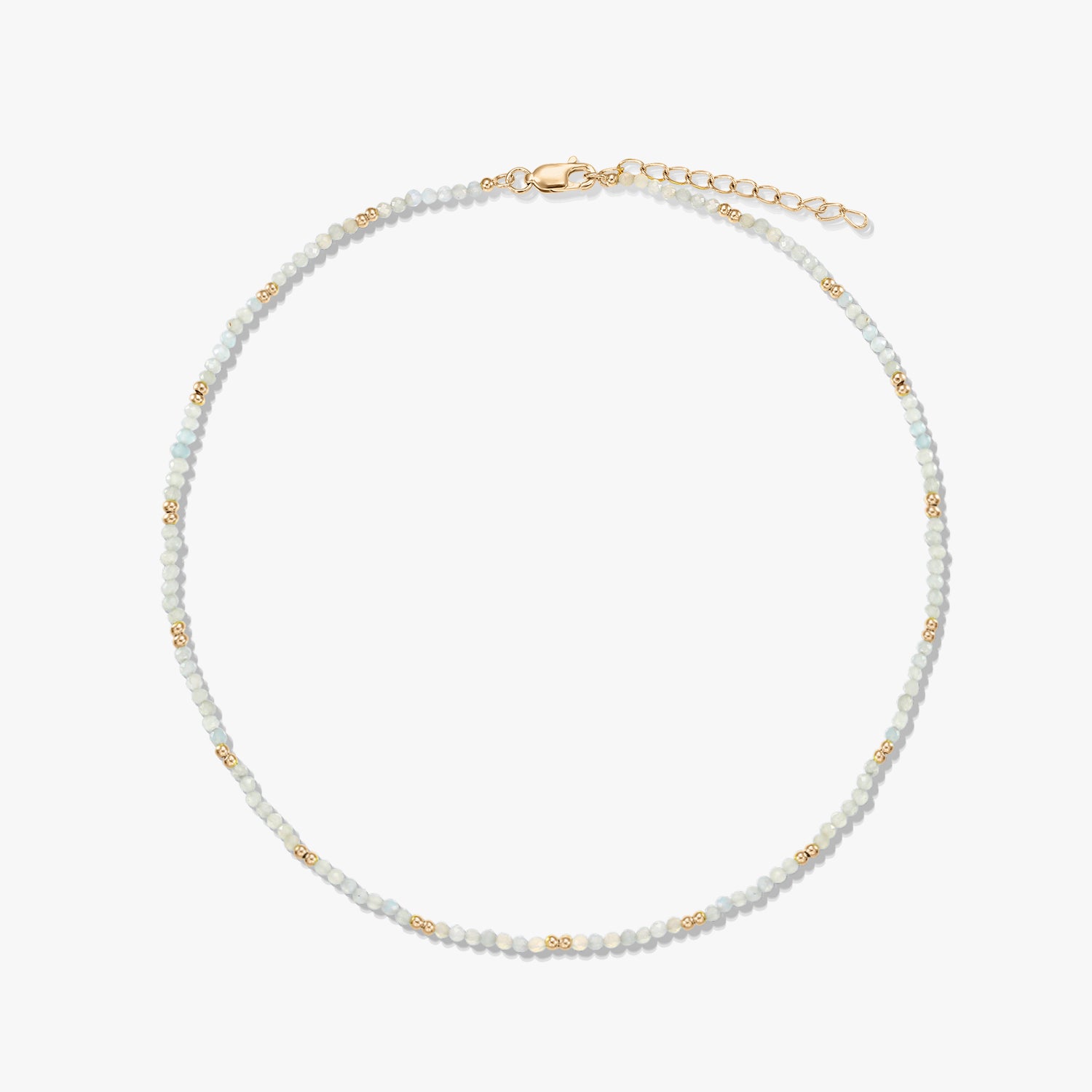 Collier délicat en perles de pierre de lune, rehaussé de petites perles intercalaires dorées, avec fermoir mousqueton et chaînette d’extension en argent sterling plaqué or, disposé en cercle sur fond blanc.