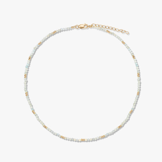 Collier délicat en perles de pierre de lune, rehaussé de petites perles intercalaires dorées, avec fermoir mousqueton et chaînette d’extension en argent sterling plaqué or, disposé en cercle sur fond blanc.