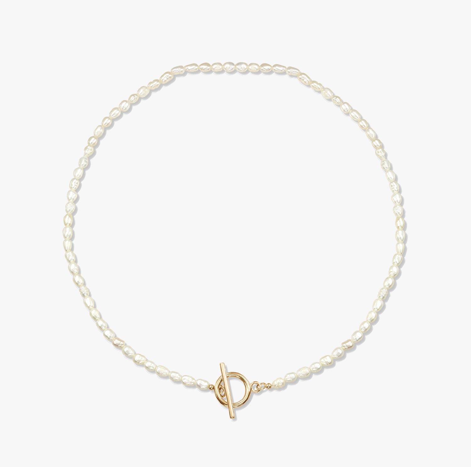 Un collier de perles minimaliste avec un fermoir toggle en or sur fond blanc.