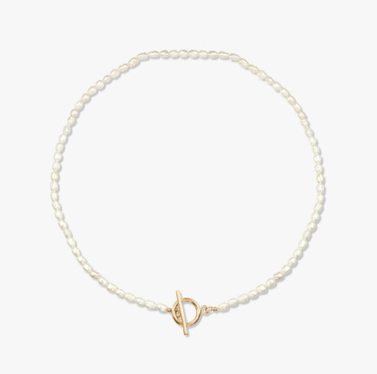 Un collier de perles minimaliste avec un fermoir toggle en or sur fond blanc.