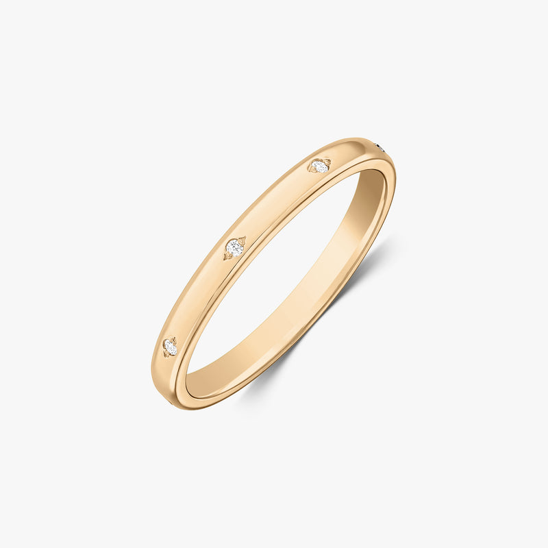 Photo de studio en angle d’une alliance fine en or jaune 14K ornée de petits diamants sertis à fleur, sur fond blanc.