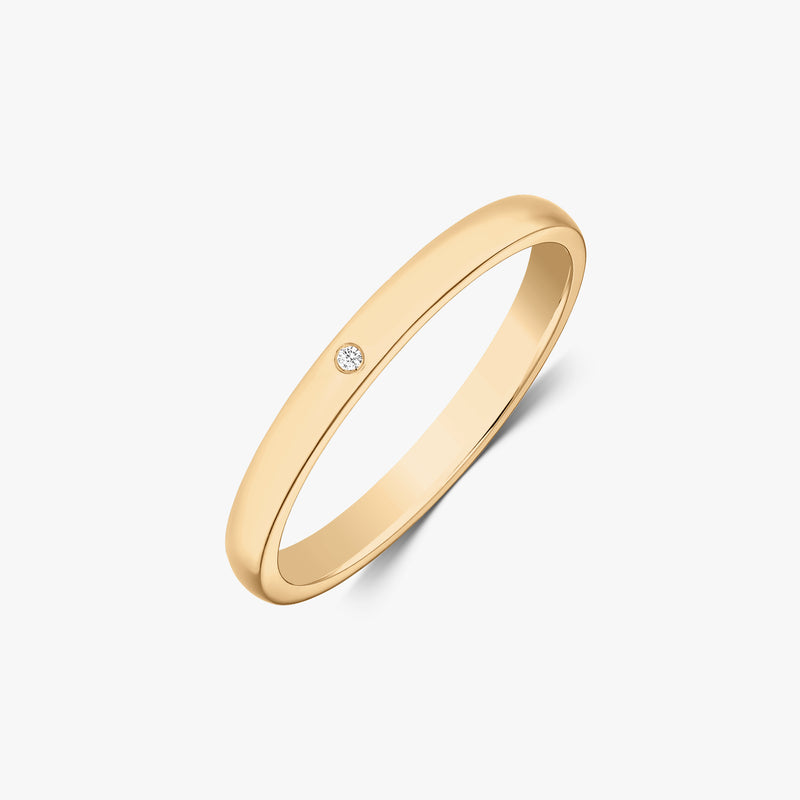Alliance fine en or jaune 14k avec un petit diamant rond serti affleurant, vue de biais sur fond blanc.