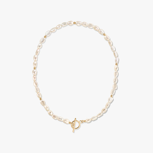 Photo studio d’un collier à rang de perles blanches naturelles, agrémenté de petites perles dorées et d’un fermoir toggle en or, sur fond blanc.