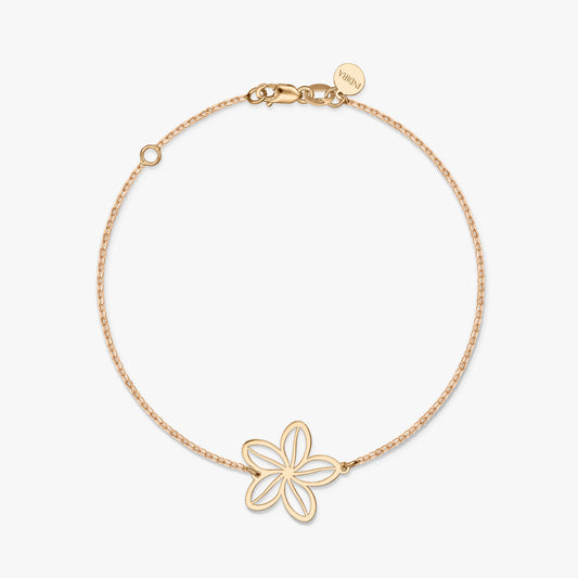 Un bracelet minimaliste en or avec un charm fleur délicat sur un fond blanc uni.