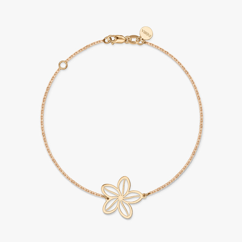 Un bracelet minimaliste en or avec un charm fleur délicat sur un fond blanc uni.