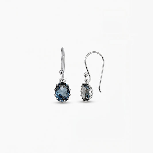 Paire de boucles d’oreilles pendantes en argent sterling avec des topazes bleu London ovales sur fond blanc.