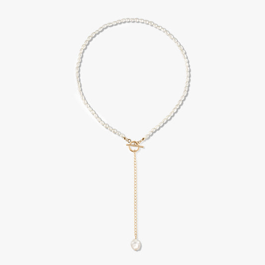 Collier Jacqueline en argent sterling plaqué or 14 carats avec perle, fermoir à bascule sur le devant et chaîne dorée se terminant par une perle unique, sur fond blanc.
