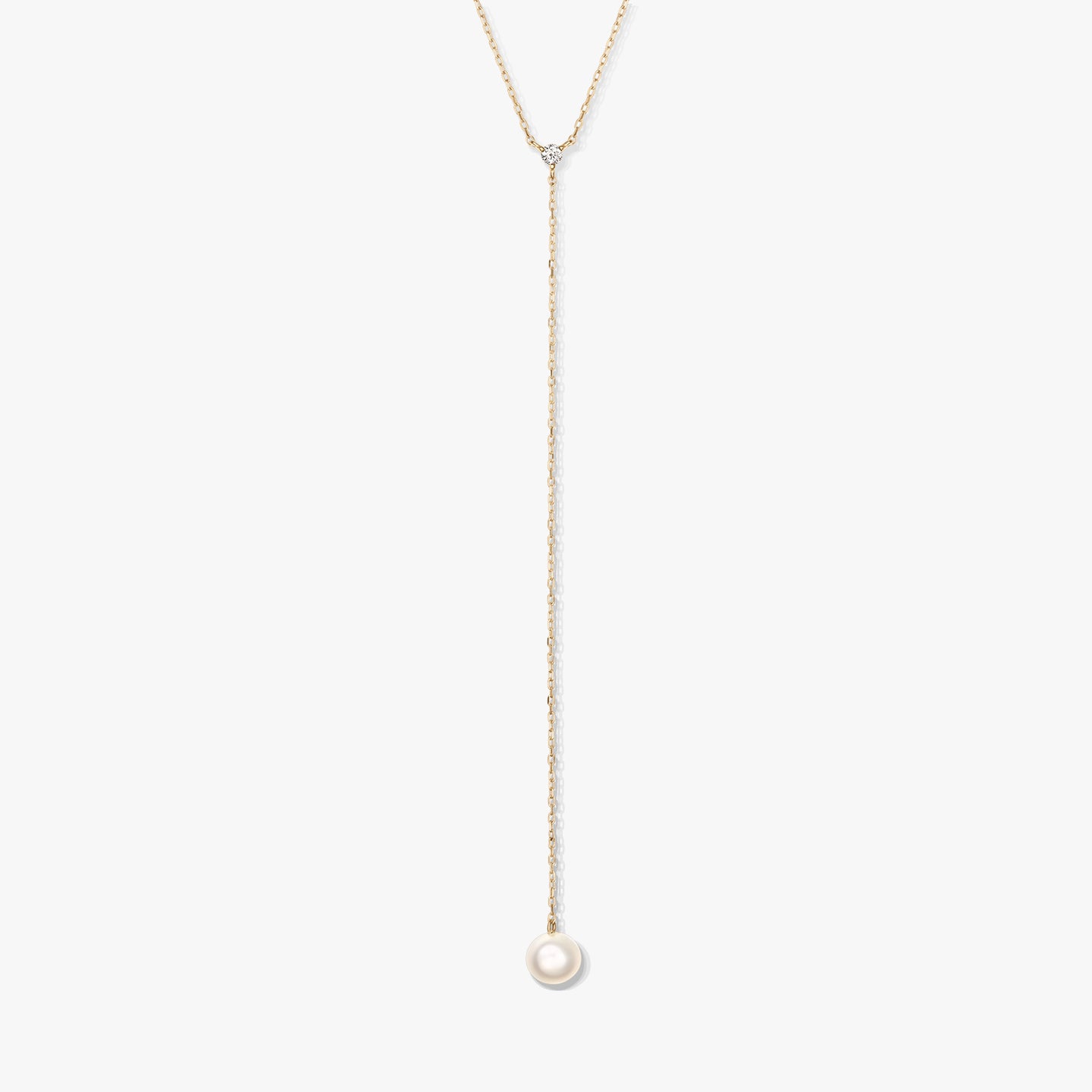 Collier lariat minimaliste en or avec une seule perle ronde blanche en pendentif et une petite pierre d’accent, centré sur un fond blanc.