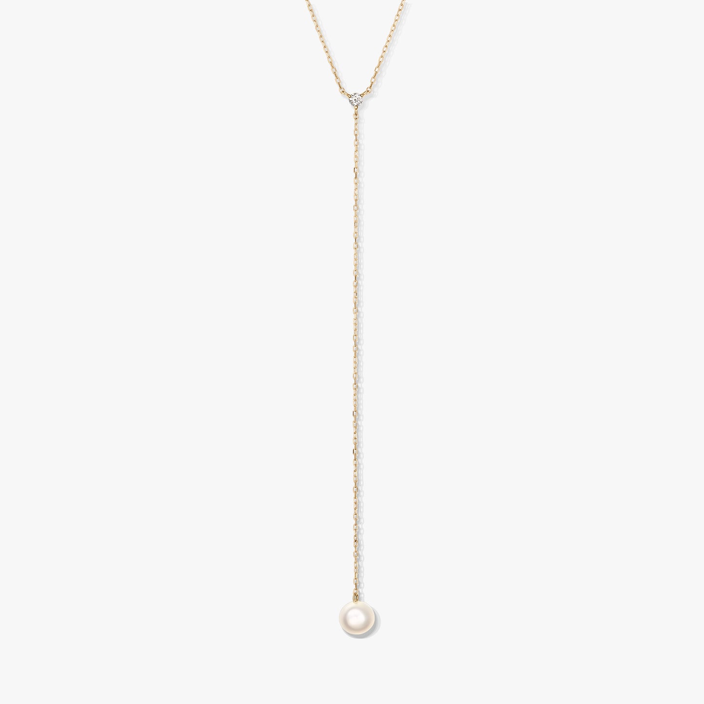 Collier lariat minimaliste en or avec une seule perle ronde blanche en pendentif et une petite pierre d’accent, centré sur un fond blanc.