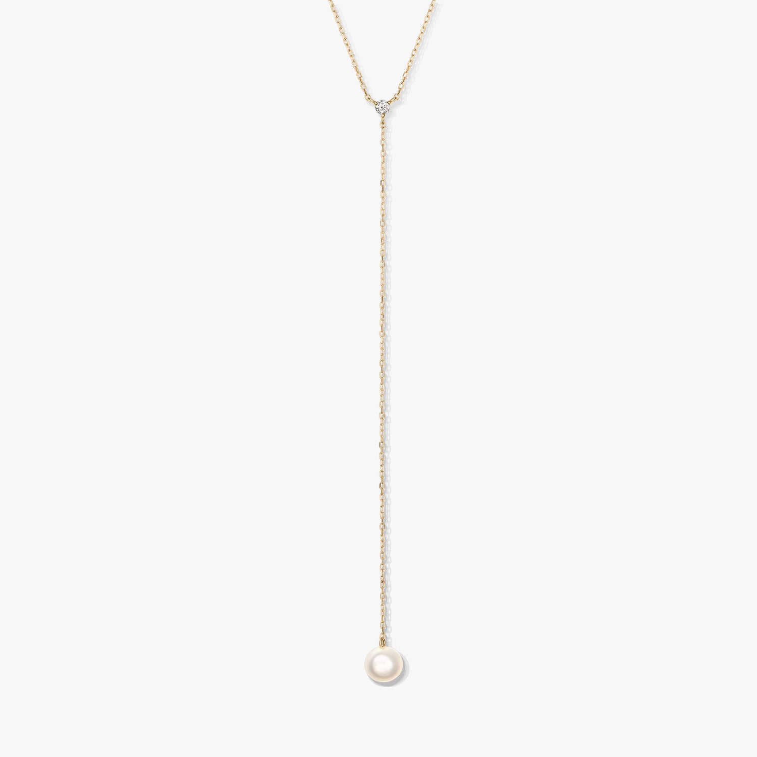 Collier lariat minimaliste en or avec une seule perle ronde blanche en pendentif et une petite pierre d’accent, centré sur un fond blanc.