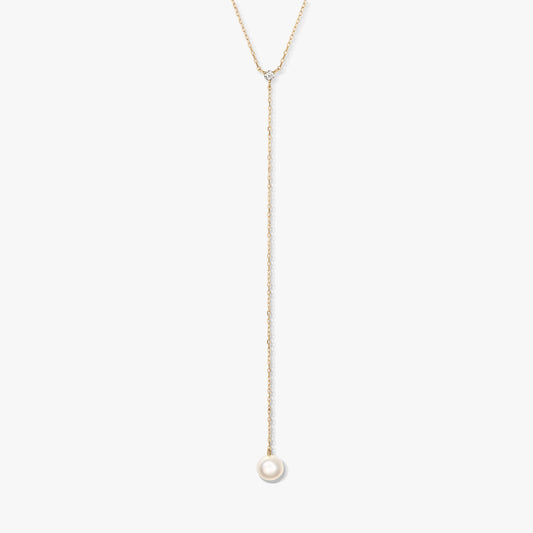 Collier lariat minimaliste en or avec une seule perle ronde blanche en pendentif et une petite pierre d’accent, centré sur un fond blanc.