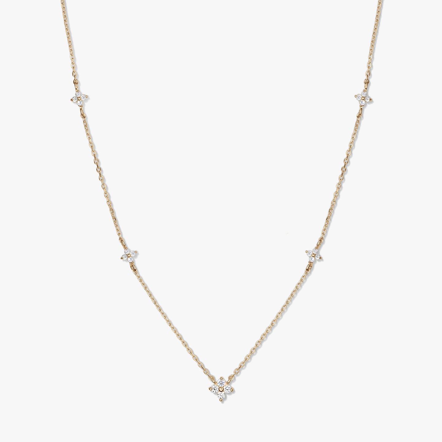 Collier délicat en or jaune 14K de type station, avec de petits motifs trèfle en zirconia blanc sur une chaîne fine, photographié sur fond blanc.