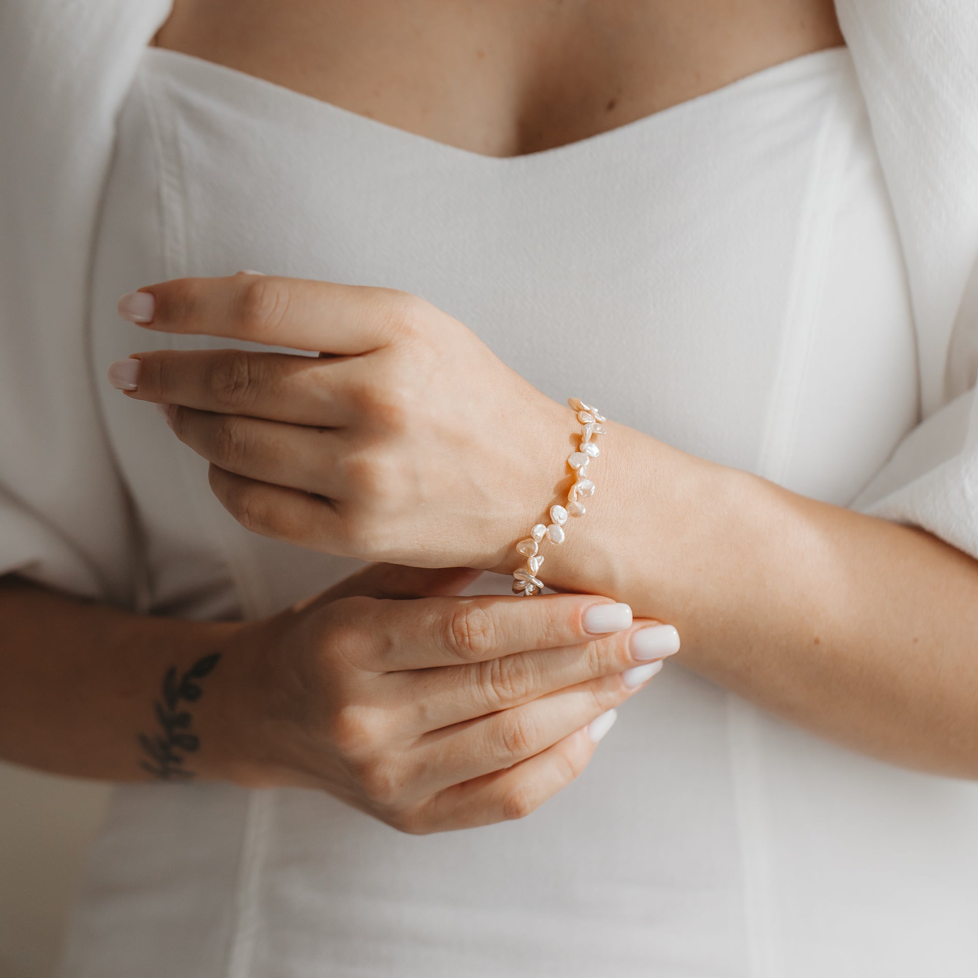 Gros plan de mains portant un bracelet délicat en argent sterling orné de perles keshi roses, assorti à une robe blanche.
