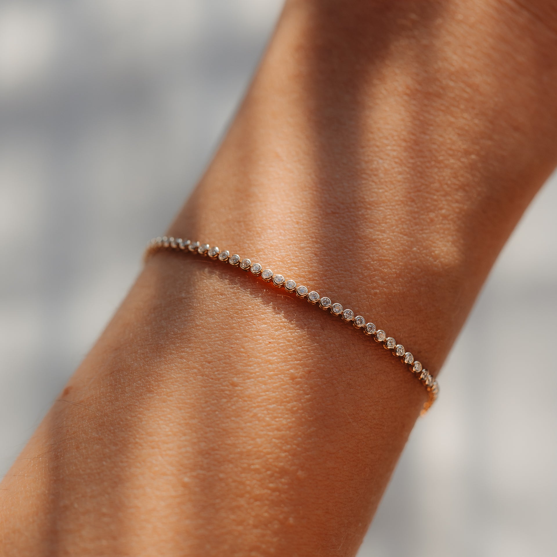 Gros plan d'un bracelet tennis raffiné en or jaune 14K, serti de petits diamants ronds, porté au poignet et baigné d'une douce lumière naturelle.
