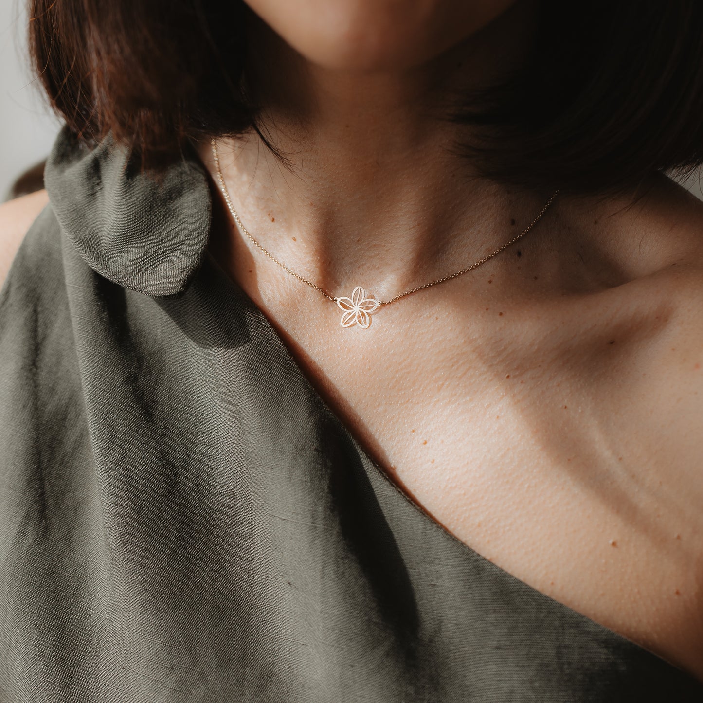 Gros plan d’un mannequin portant le collier Wildflower en or jaune 14K, avec un pendentif délicat au contour de fleur, visible au niveau de la clavicule sous une lumière naturelle.