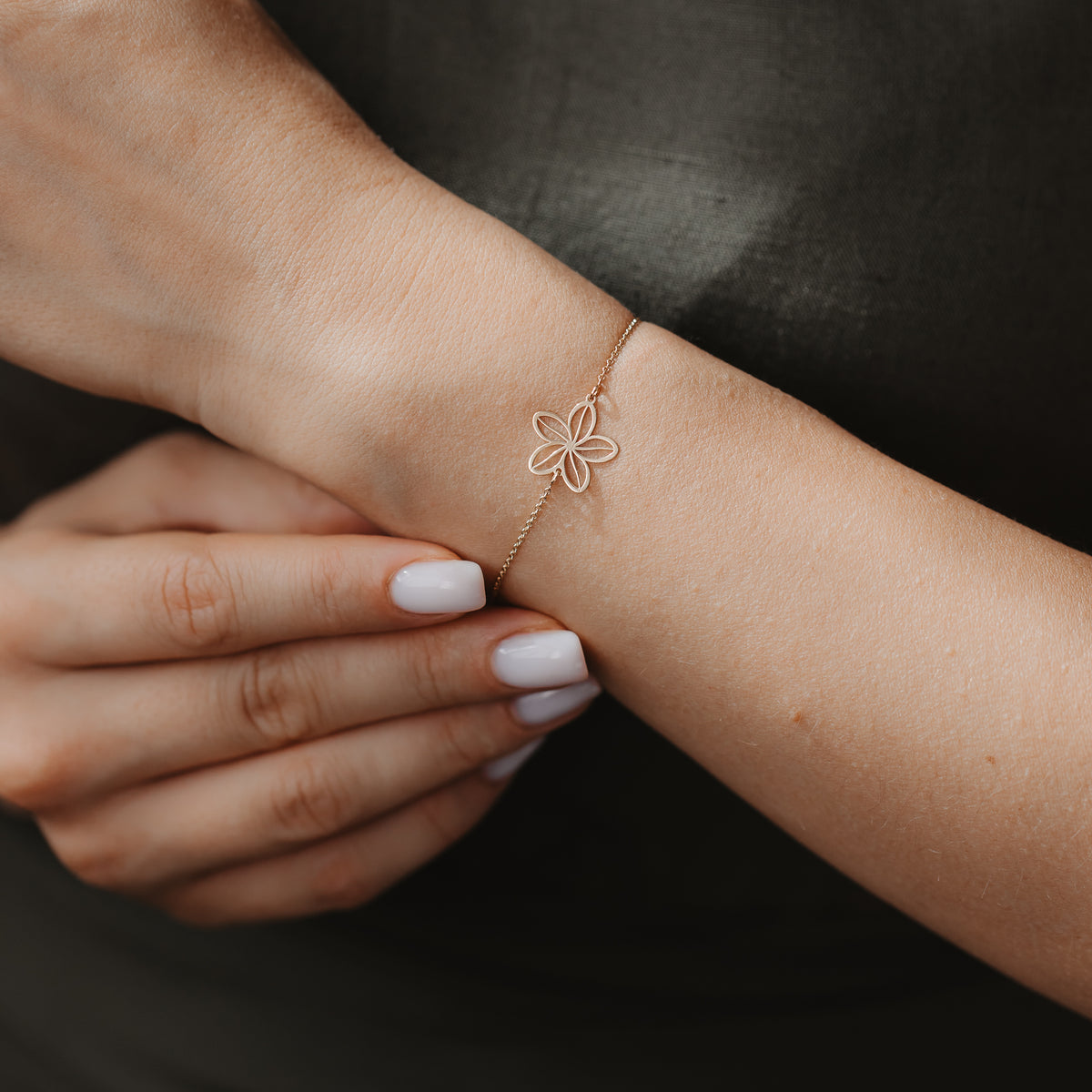 Gros plan d'un bracelet délicat en or 14K, orné d'une breloque fleur sauvage ajourée, au poignet, sur un fond de tissu sombre.