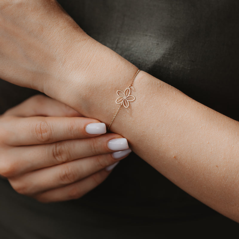 Gros plan d'un bracelet délicat en or 14K, orné d'une breloque fleur sauvage ajourée, au poignet, sur un fond de tissu sombre.