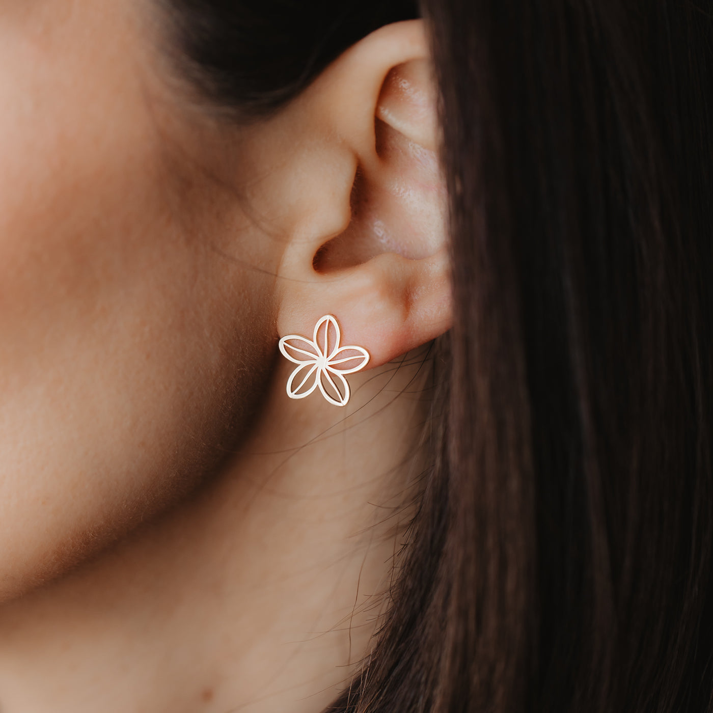 Gros plan sur une oreille portant un clou d'oreille en forme de fleur ajourée en or jaune 14K, délicat.