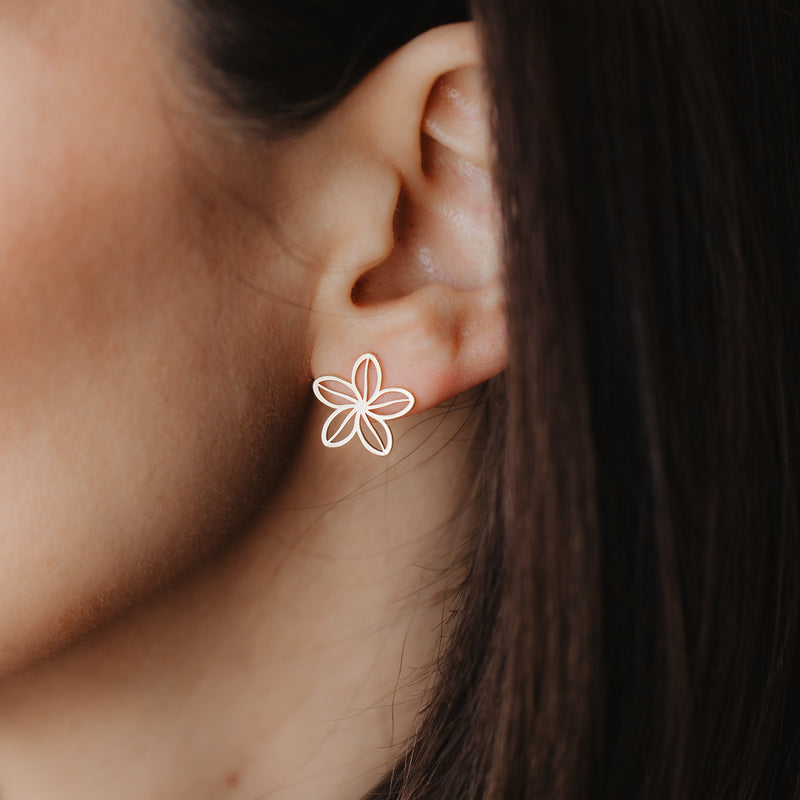 Gros plan sur une oreille portant un clou d'oreille en forme de fleur ajourée en or jaune 14K, délicat.