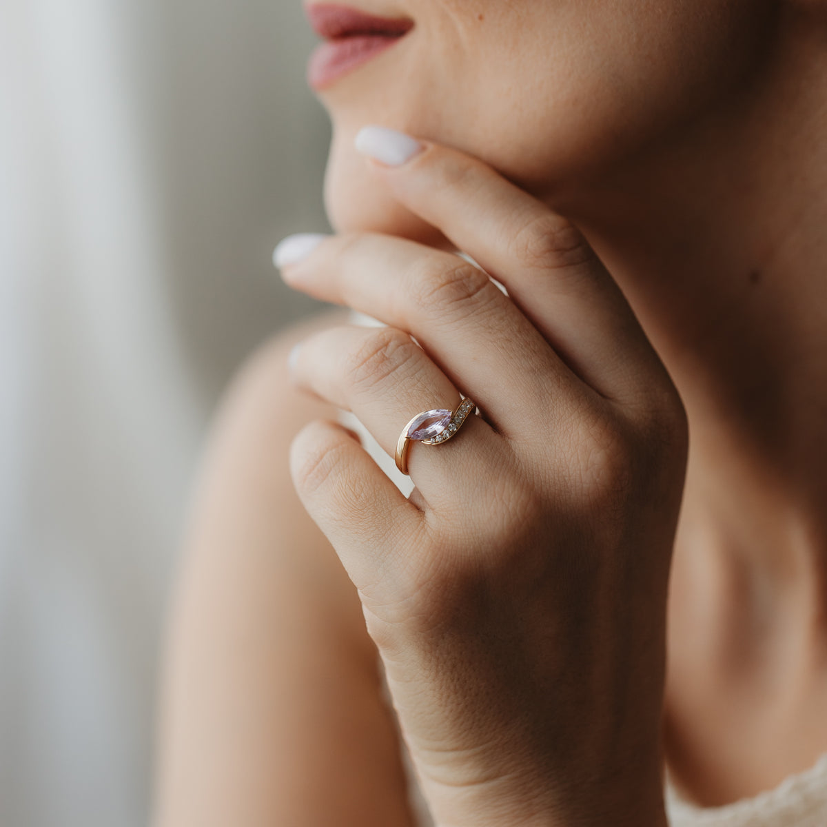 Gros plan d’une main près du visage portant la bague Velvet Rose en or jaune 14 K, sertie d’un saphir rose taille marquise et de petits diamants d’accent.