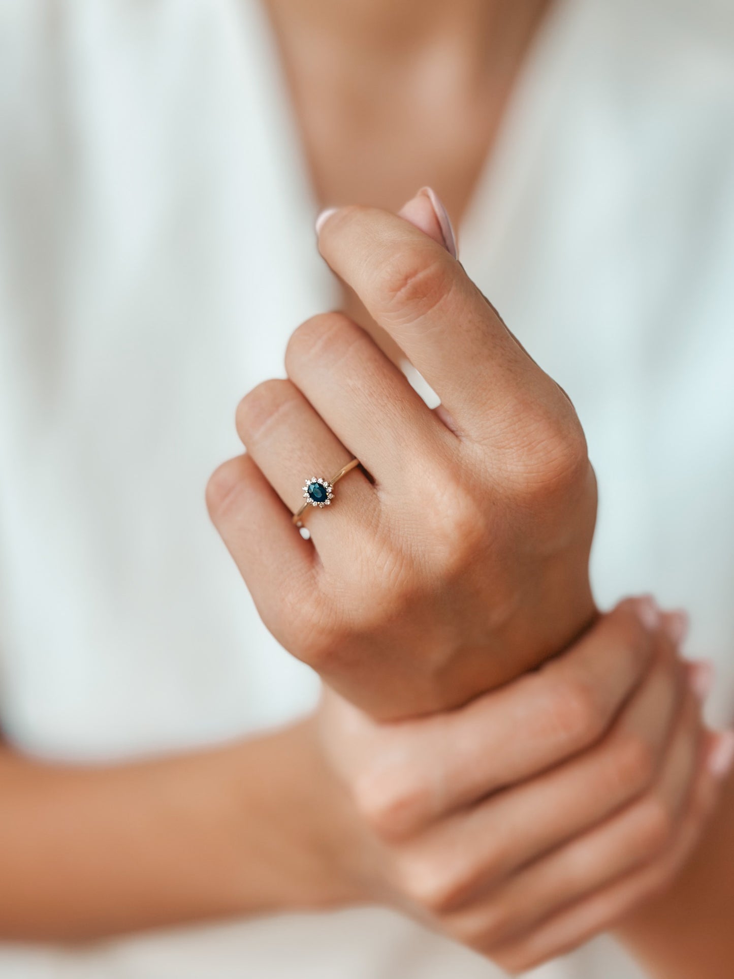 Gros plan sur une main portant une bague Genn en or ornée de saphirs et de diamants.